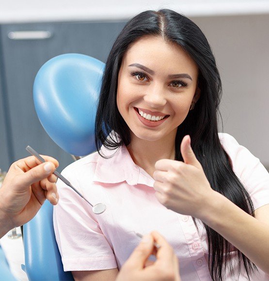 Smiling woman in dental chair giving a thumbs up