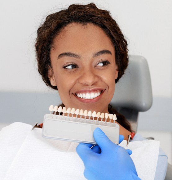 Woman's smile compared with porcelain veneer color chart during cosmetic dentistry visit