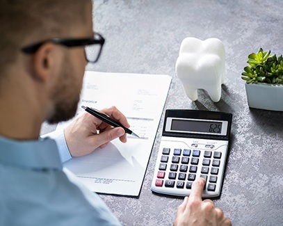 Man using calculator next to a model tooth