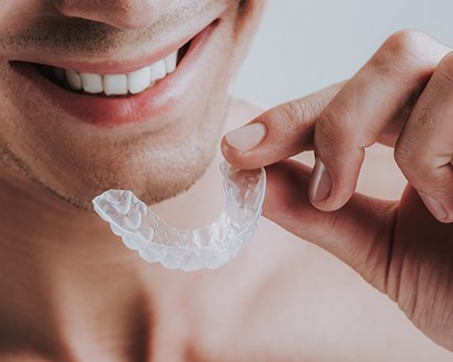 man smiling while holding mouthguard