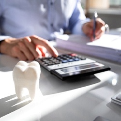 Dentist with calculator calculating the cost of dental implants in Tucson