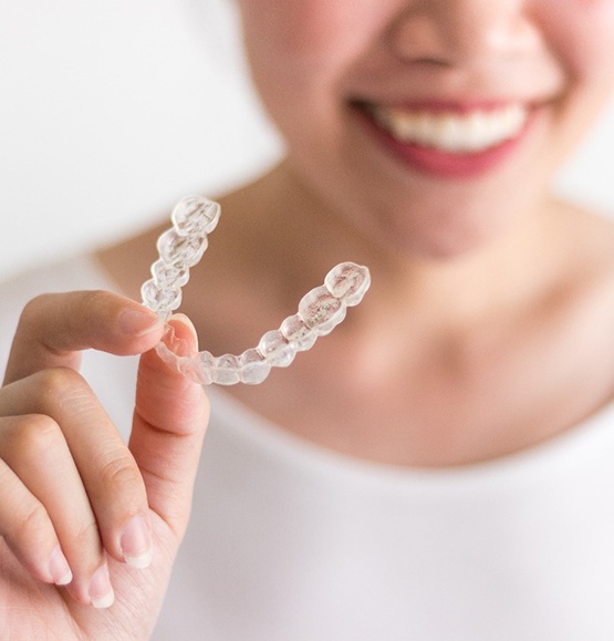 woman smiling while holding up Invisalign aligner