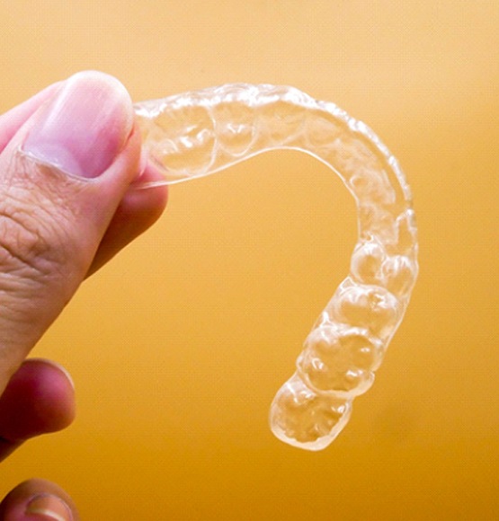 Close up of clear aligner being held with a gold background