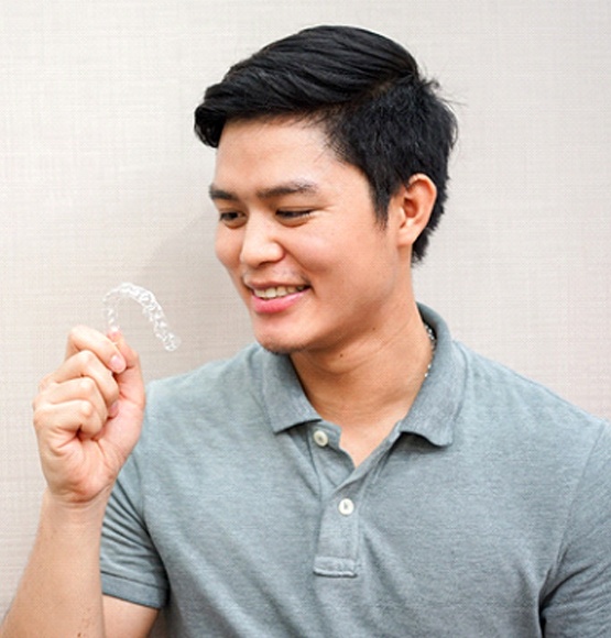 Man in grey polo holding a clear aligner while looking at it