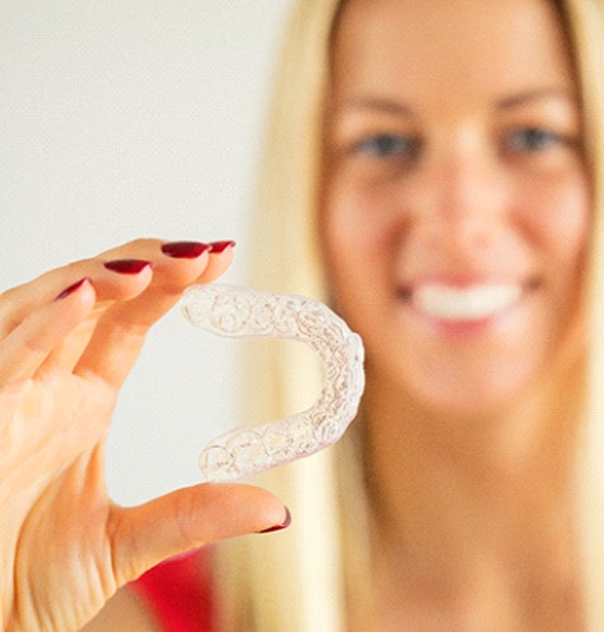 Woman with blonde hair holding a clear aligner with focus on aligner