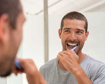 Man brushing his teeth in front of bathroom mirror