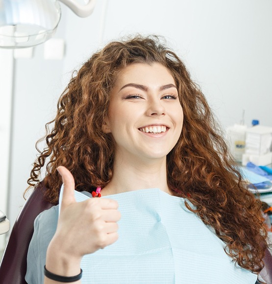 Woman sitting in dental chair giving a thumbs up