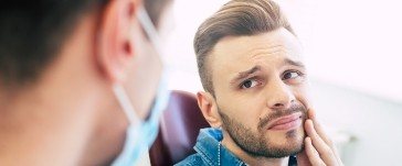 Man in need of emergency dentistry holding cheek