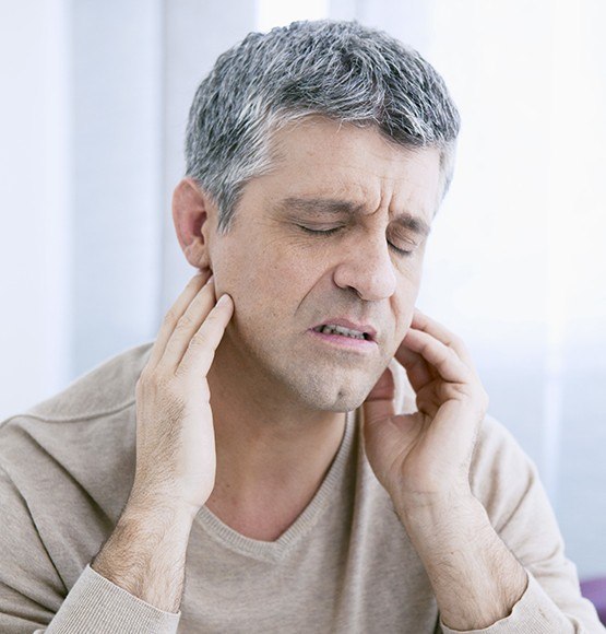 Man in need of T M J therapy holding his jaw