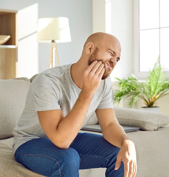 a young adult experiencing wisdom tooth pain while they’re sitting on a couch