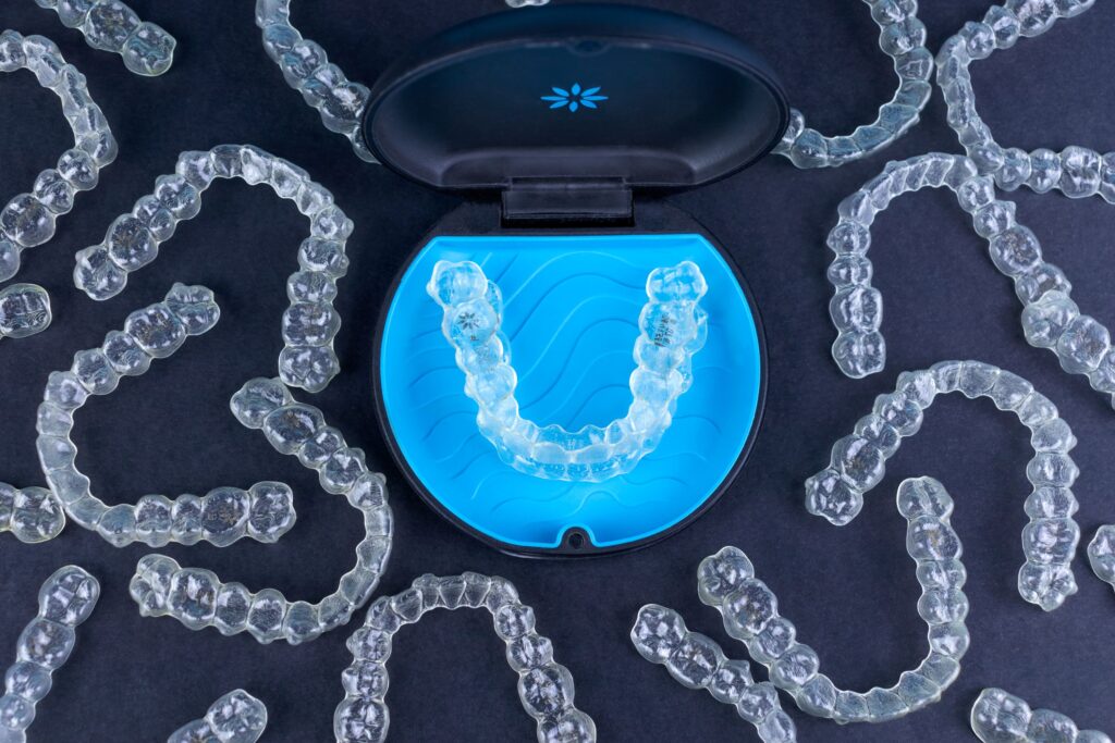 Bird's eye view of several Invisalign trays surrounding carrier case on black surface