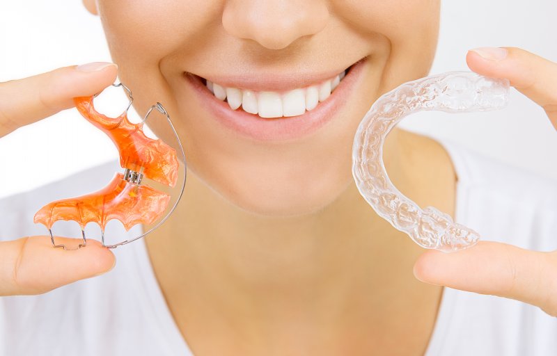 A smiling woman holding a retainer and an Invisalign tray