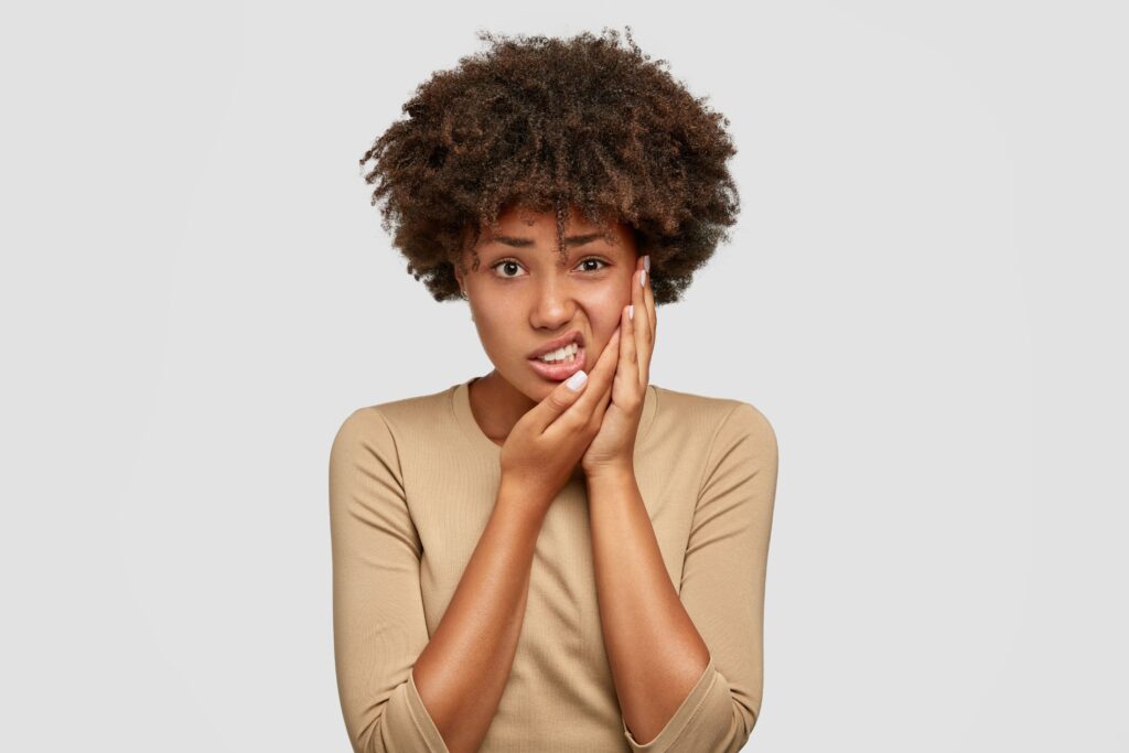 Woman in brown shirt holding two hands to jaw in pain